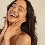 Beautiful laughing woman touching her skin with joy