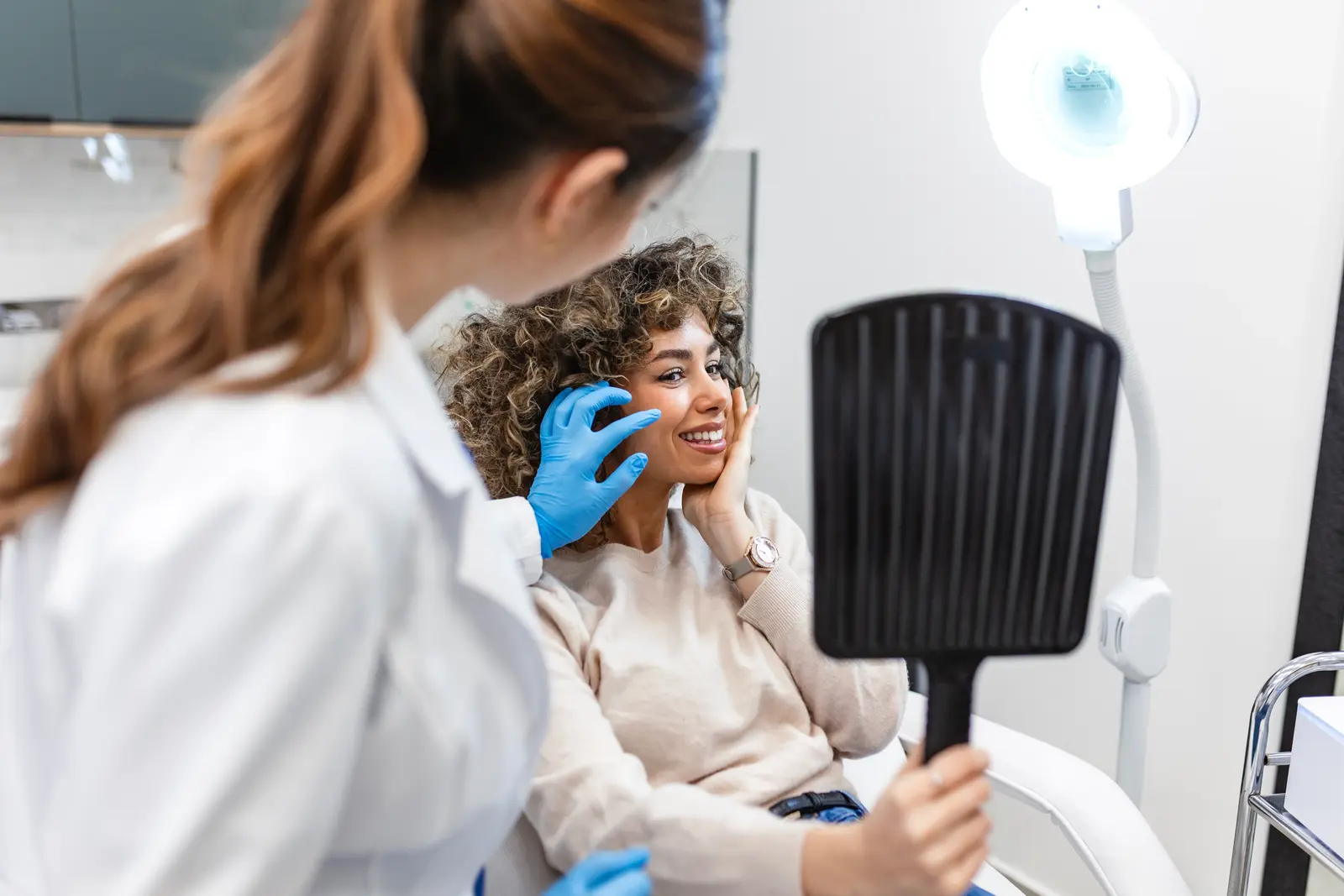 Woman in medspa holding mirror, smiling after cosmetic treatment
