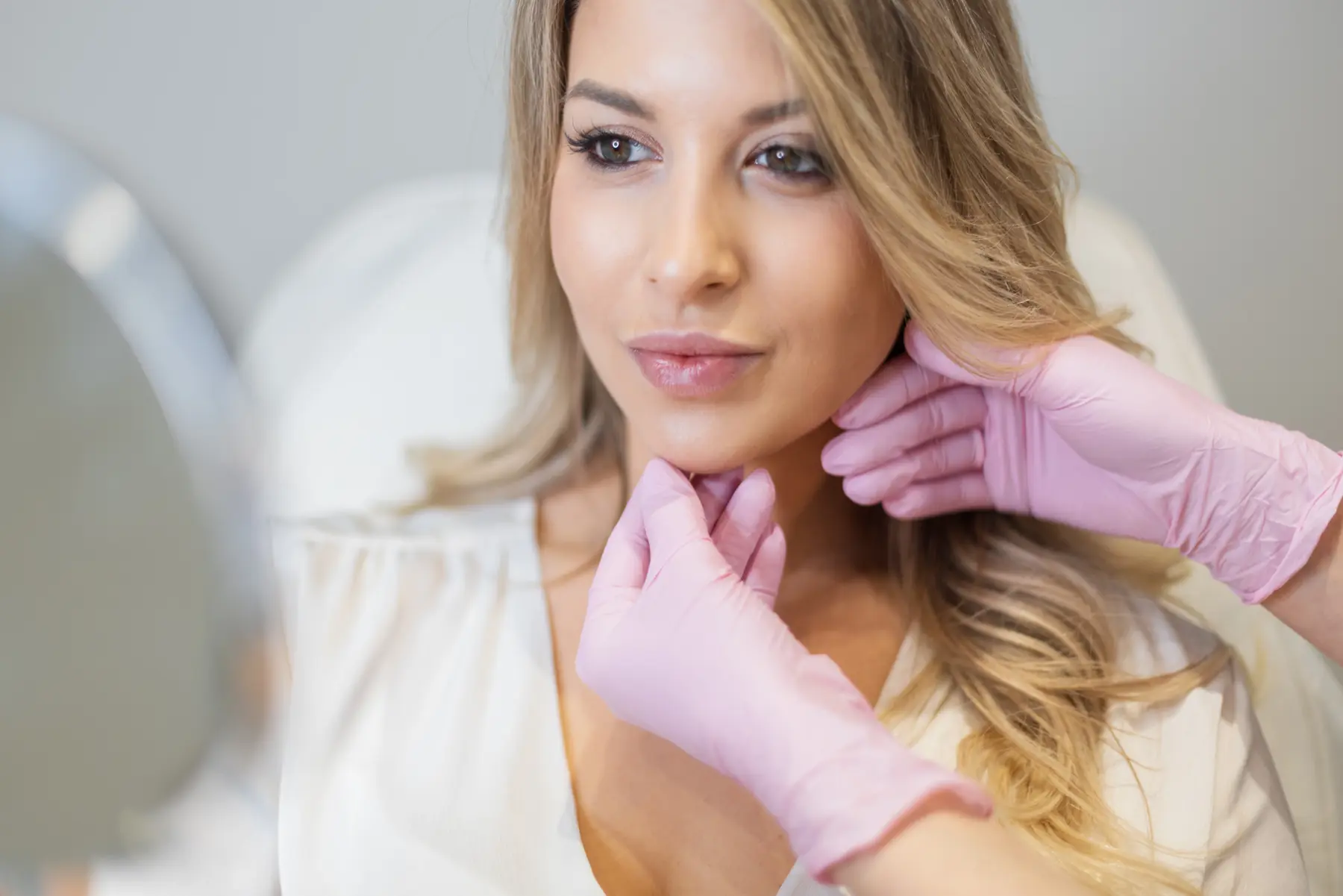 Woman receiving facial consultation at a medspa, pink gloves touching face.